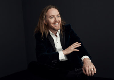 An image of Tim Minchin sitting on a chair, posing for a photo