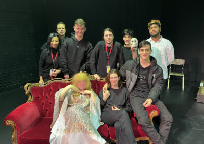 Cracked Actors students and staff posing around a couch, on stage, posing for photo post-play