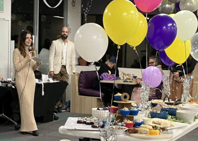 A grazing table with balloon decorations around it with speeches happening to the left