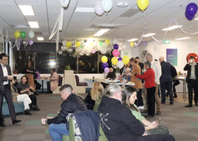 A wide-shot of the room decorated with balloons and streamers featuring a grazing table in the centre with people all around